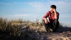 man kneeling down in sand looking off into the distance